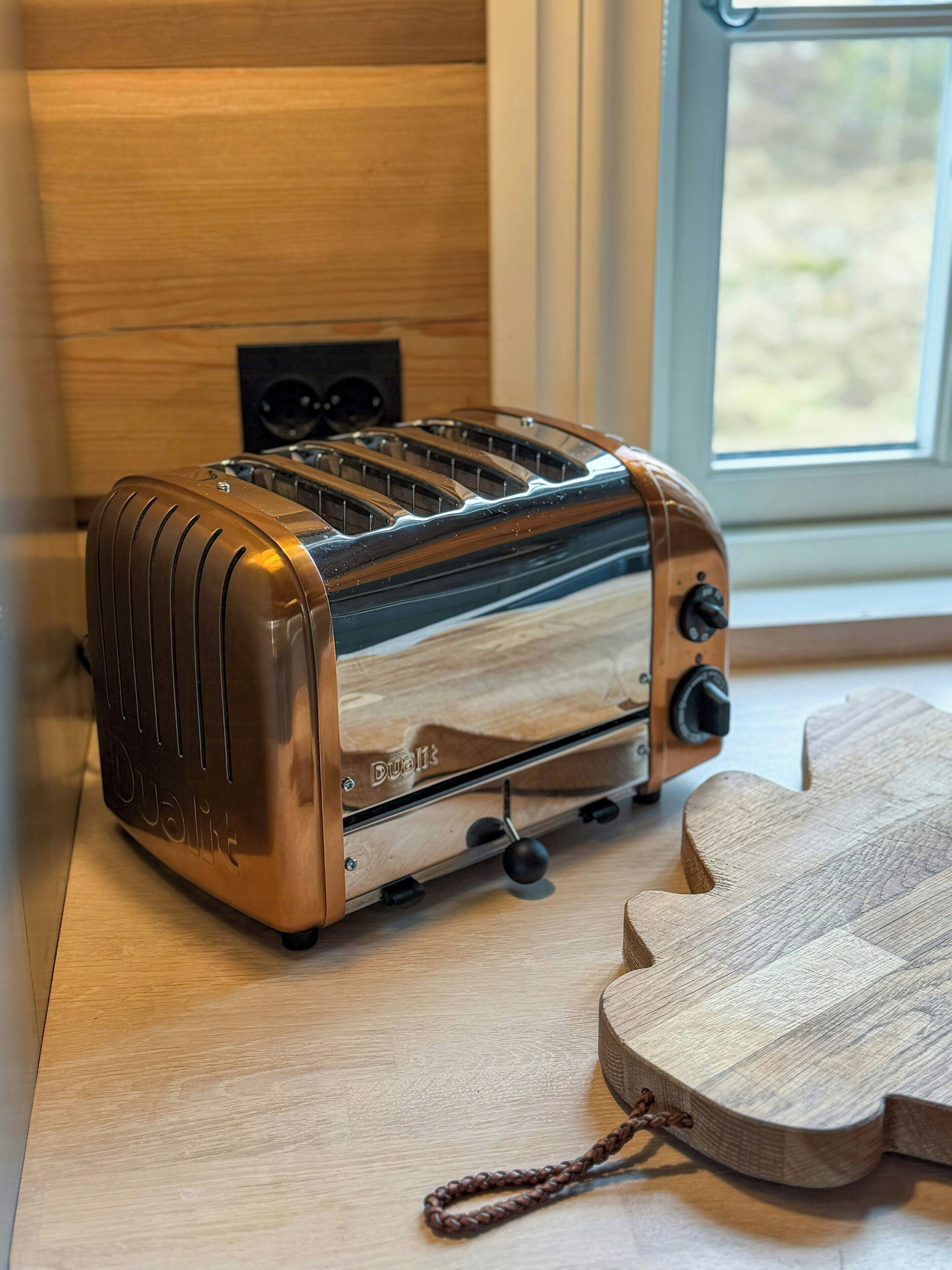 A stainless steel toaster on a wooden countertop with a window in the background.