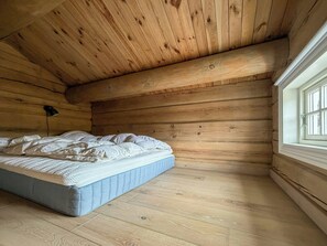 A bedroom with a wooden ceiling, a single bed, a window, and a lamp.