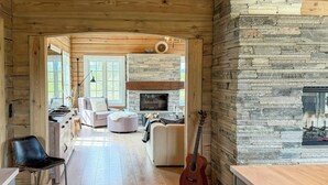 Een ruime woonkamer met een open haard, houten vloeren en een gitaar die tegen de muur staat.