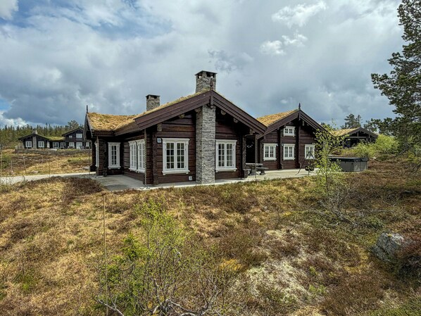A log cabin with a stone chimney, a stone foundation, and a thatched roof.