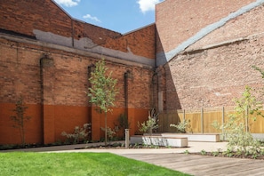 A courtyard with brick walls, a wooden deck, and small trees. - Spacious 3BR Near Bullring | StayCozy (Birmingham)