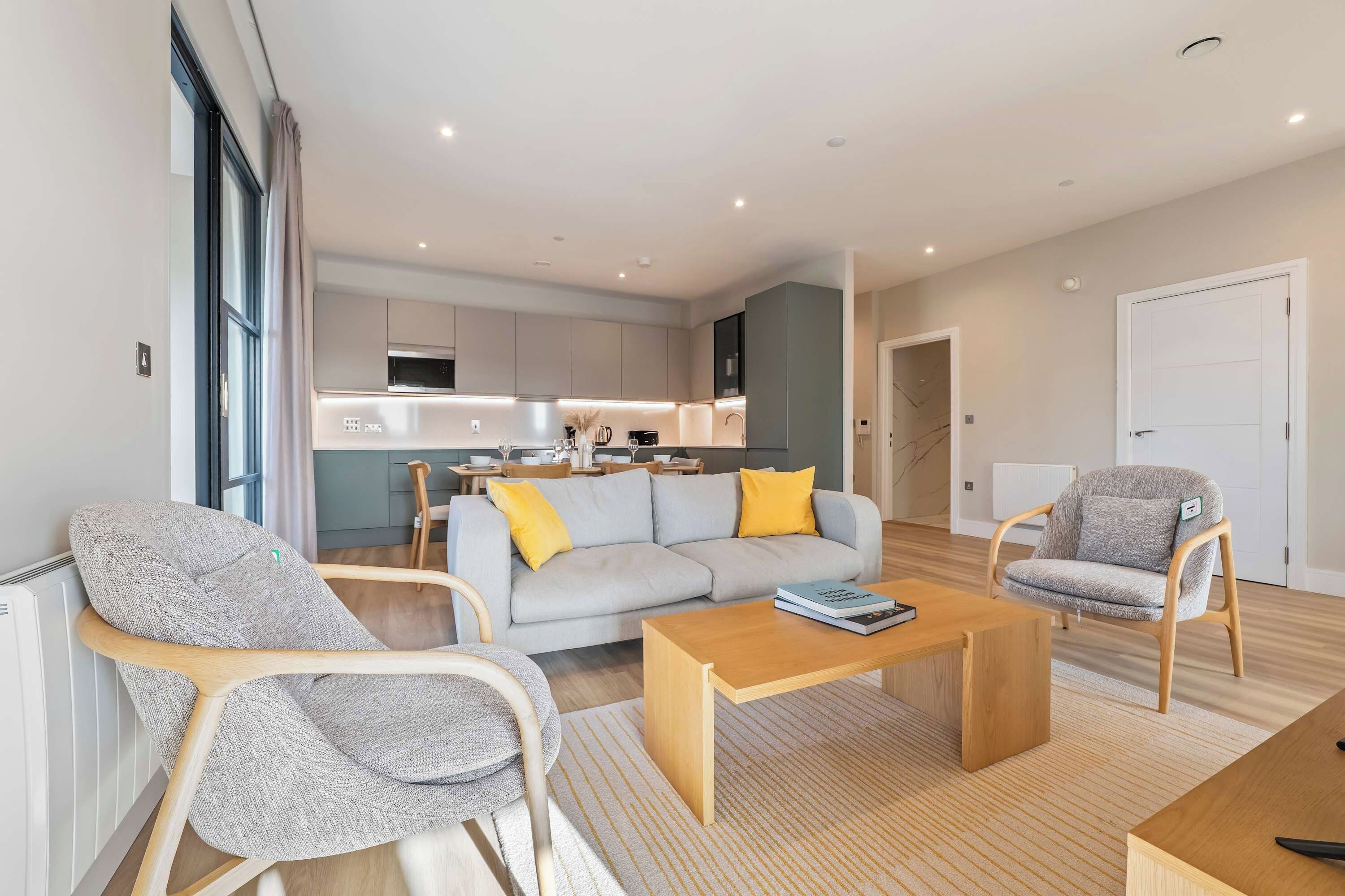 Ein modernes Wohnzimmer mit einer Couch, zwei Sesseln, einem Couchtisch und einer Küche im Hintergrund.