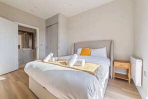 Ein modernes Hotelzimmer mit einem großen Bett, einem Nachttisch, einem Heizkörper und einem durch eine offene Tür einsehbarer Badezimmer.