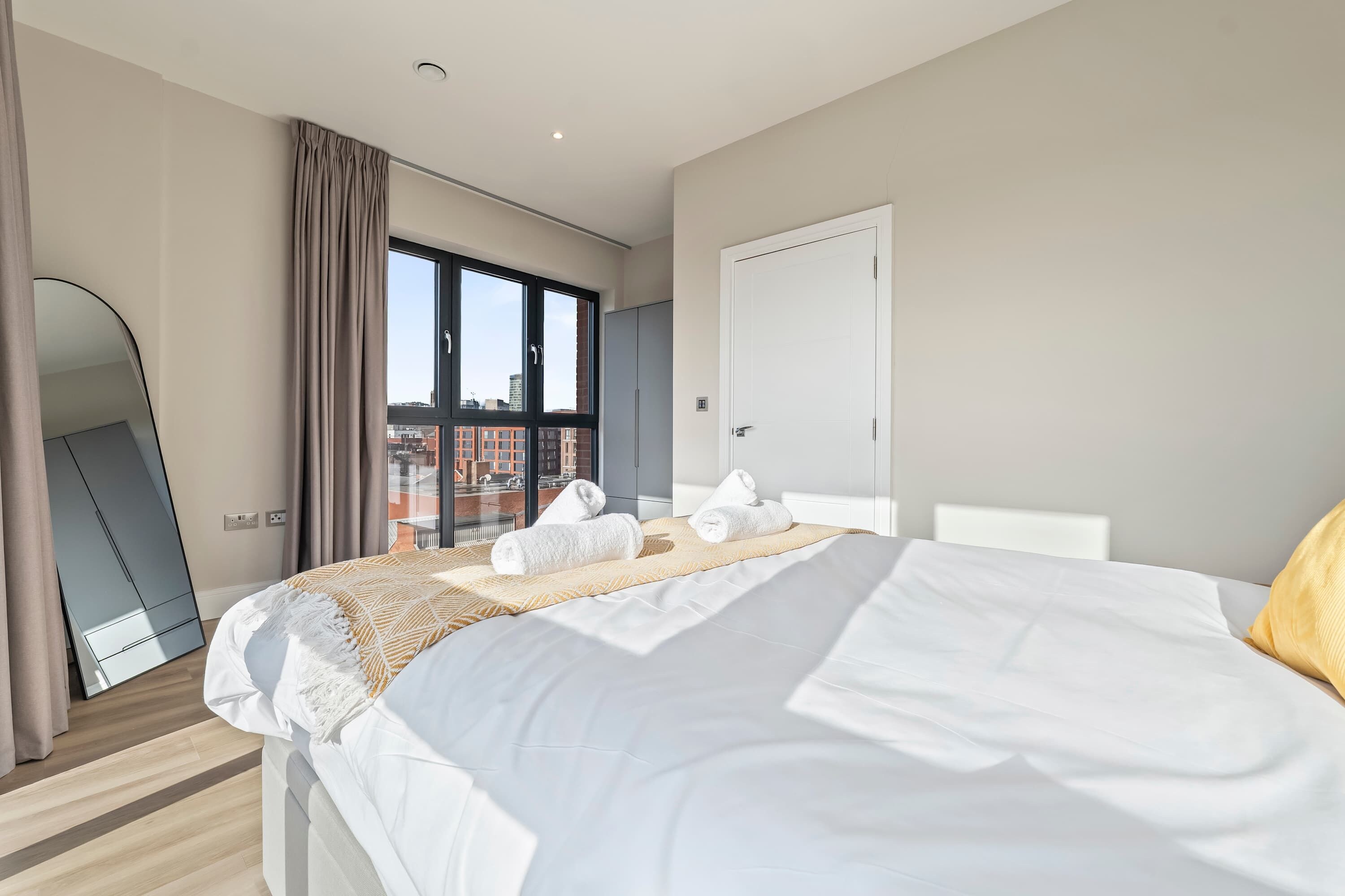 Una moderna camera d'albergo con un letto grande, vista sulla città attraverso finestre a tutta altezza e uno specchio su una parete.