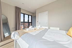 Une chambre d’hôtel moderne avec un grand lit, une vue sur la ville grâce à de grandes fenêtres du sol au plafond et un miroir sur l’un des murs.