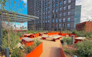 Un jardin sur le toit, agrémenté d’espaces aménagés pour s’asseoir, et entouré de grands immeubles.