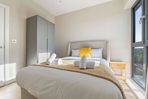 A bedroom with a bed, a wardrobe, a bedside table, and a window. - Spacious 3BR Near Bullring | StayCozy (Birmingham)