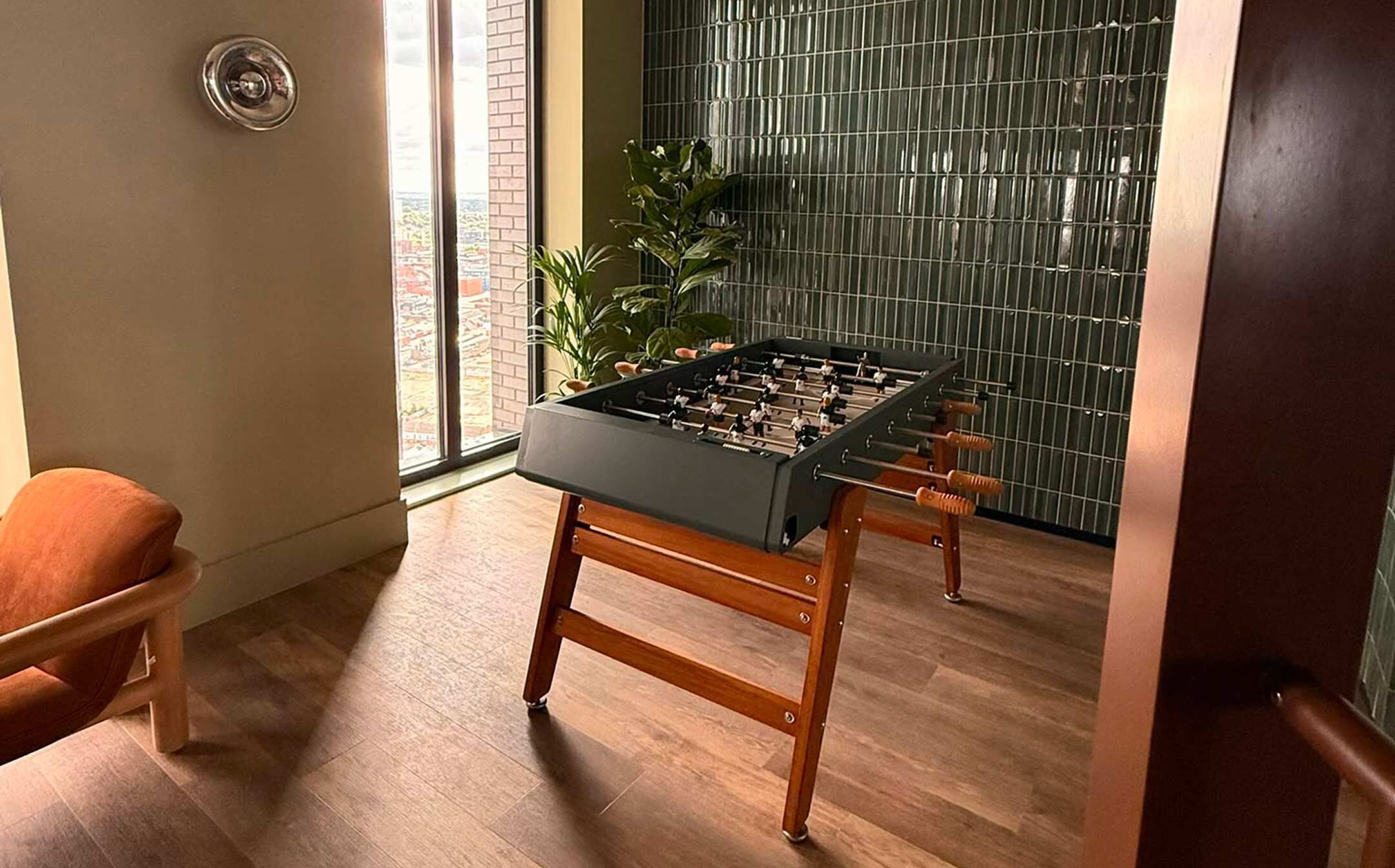 Una habitació amb una taula de futbolí, una cadira de fusta i una vista per la finestra.