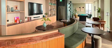 A modern lounge area with a curved wooden reception desk, a flat-screen TV, and a pool table.