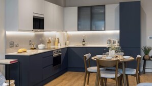 A modern kitchen with a central island, built-in oven, and a dining area with a round table and chairs. - Spacious 3BR Near Bullring | StayCozy (Birmingham)