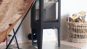 A modern living room with a black wood-burning stove, a wooden chair, a map on the wall, and a wicker basket with logs. - Modern flat in Kabelvåg, Lofoten (Nordland)