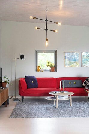 A modern living room with a red sofa, a round coffee table, a floor lamp, and a ceiling light fixture.