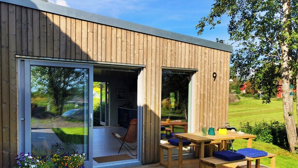 A modern house with a wooden exterior, a sliding glass door leading to an outdoor deck, and a small patio area with a table and chairs. - Modern flat in Kabelvåg, Lofoten (Nordland)