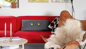 A red sofa with a grey pillow, a wooden chair with a fur throw, a small round table with books and candles, and two framed landscape paintings on the wall. - Modern flat in Kabelvåg, Lofoten (Nordland)