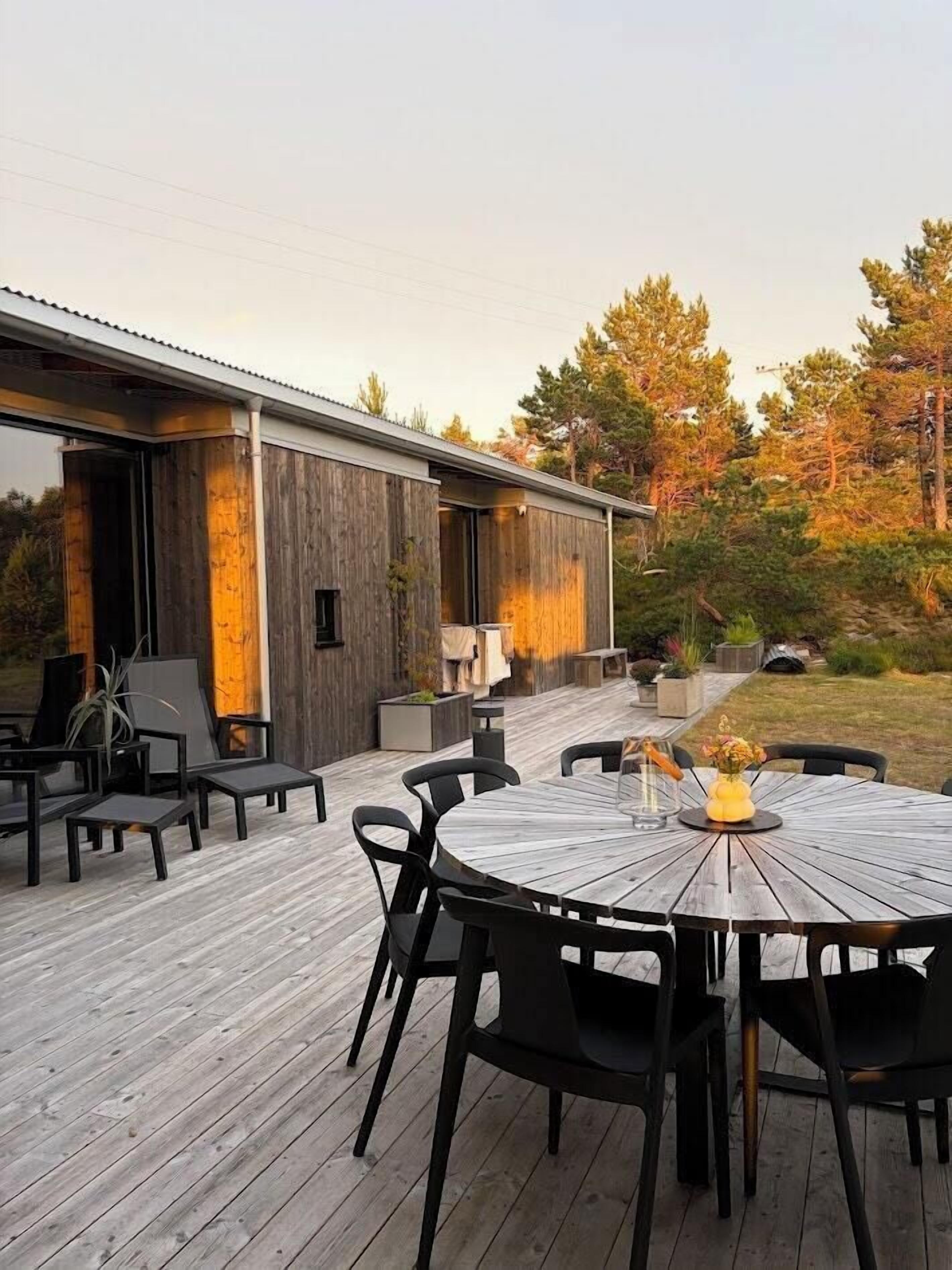An outdoor deck with a round table and chairs, a wooden deck, and a modern building with a glass door.