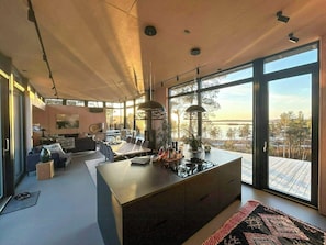 A modern interior with a dining area, kitchen, and large windows offering a view of the outdoors.