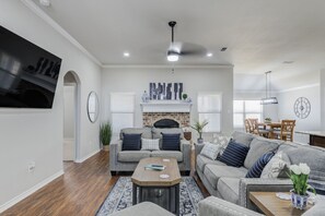 A living room with a fireplace, a dining area with wooden furniture, and a TV mounted on the wall. - Bogey`s House - 3BR/2BA Brand New Listing (Lubbock)