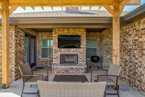 A covered outdoor patio with a brick fireplace, wicker furniture, and a grill. - Bogey`s House - 3BR/2BA Brand New Listing (Lubbock)