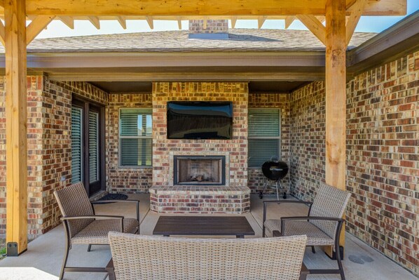 A covered outdoor patio with a brick fireplace, wicker furniture, and a grill. - Bogey`s House - 3BR/2BA Brand New Listing (Lubbock)