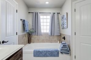 A bathroom with a bathtub, a window with curtains, a sink, and towels. - Bogey`s House - 3BR/2BA Brand New Listing (Lubbock)