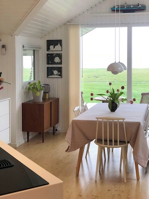 A dining area with a table set for four, a wooden cabinet, and a view of a green field through large windows. - Nordals home with panoramic views of Lillebaelt (Nordborg)