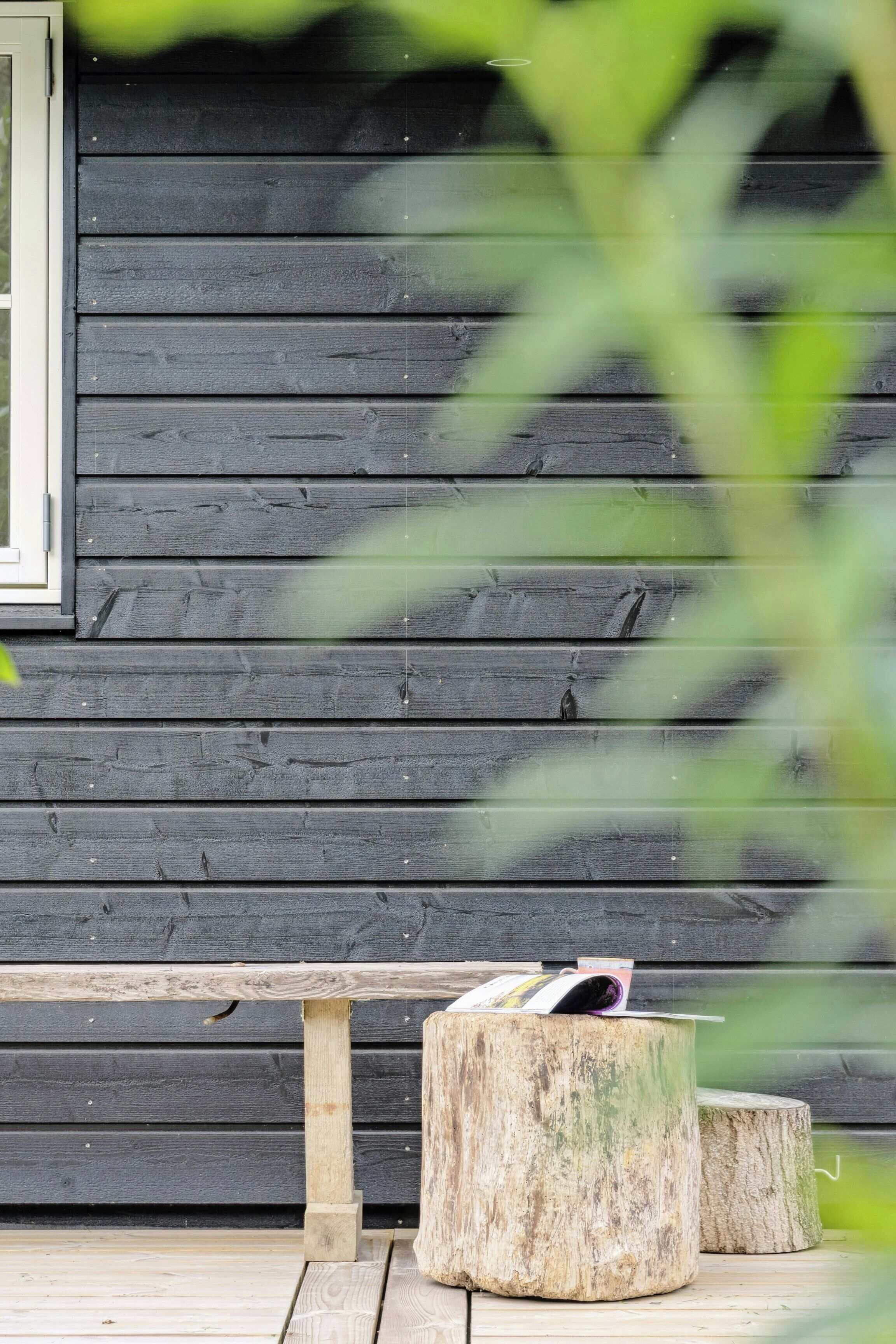 A wooden bench and two tree stump stools against a dark wooden wall.