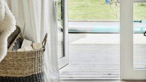 Ein Zimmer mit einer großen Schiebeglasdoor, die auf eine Terrasse mit Blick auf einen Garten und ein Schwimmbad führt.