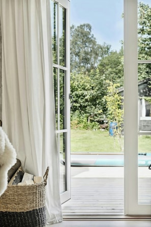 Ein Zimmer mit einer großen Schiebeglasdoor, die auf eine Terrasse mit Blick auf einen Garten und ein Schwimmbad führt.