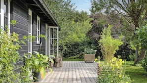 Eine Holzterrasse mit Garten, ein Holzhaus und ein großer Baum.