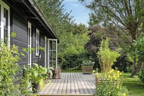 Eine Holzterrasse mit Garten, ein Holzhaus und ein großer Baum.