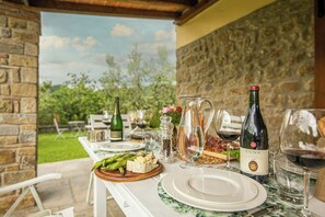 Ein Essbereich im Freien mit einer Steinsäule, einem gedeckten Tisch, einer Flasche Cuna-Wein, einer Karaffe und einem Glas Rotwein.