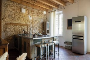 Eine Küche mit Steinwand, Holzbalken, einem Edelstahlkühlschrank und einer Bar mit Barhocker.