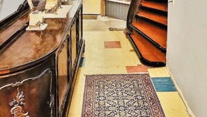 Ein Flur mit einer Holztreppe, einer Chandelieber, Wandleuchtern und einem gemusterten Teppich.