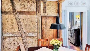 Ein Essbereich mit rustikaler Holzwand, einem Tisch mit weißer Tischdecke, Stühlen, einer Vase mit Blumen und einer schwarzen Pendelleuchte.