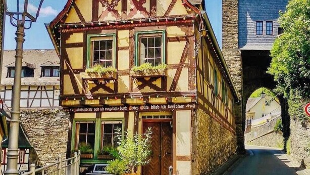 Ein traditionelles Fachwerkhäuschen mit steilem Satteldach, einem Stein-Turm und einem Schild, das ein Restaurant anzeigt.
