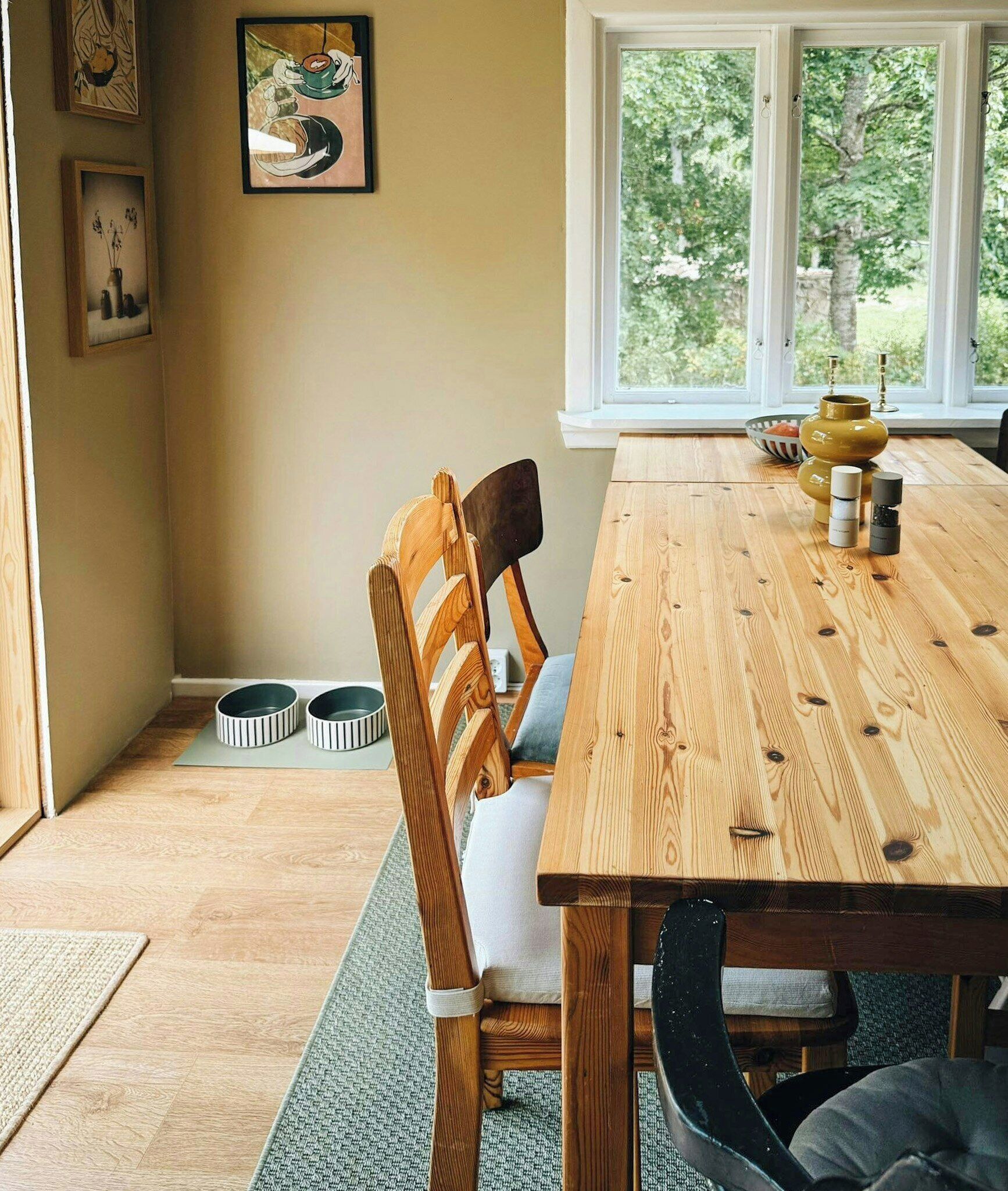Un comedor con una mesa de madera, sillas y cuencos para mascotas en el suelo.
