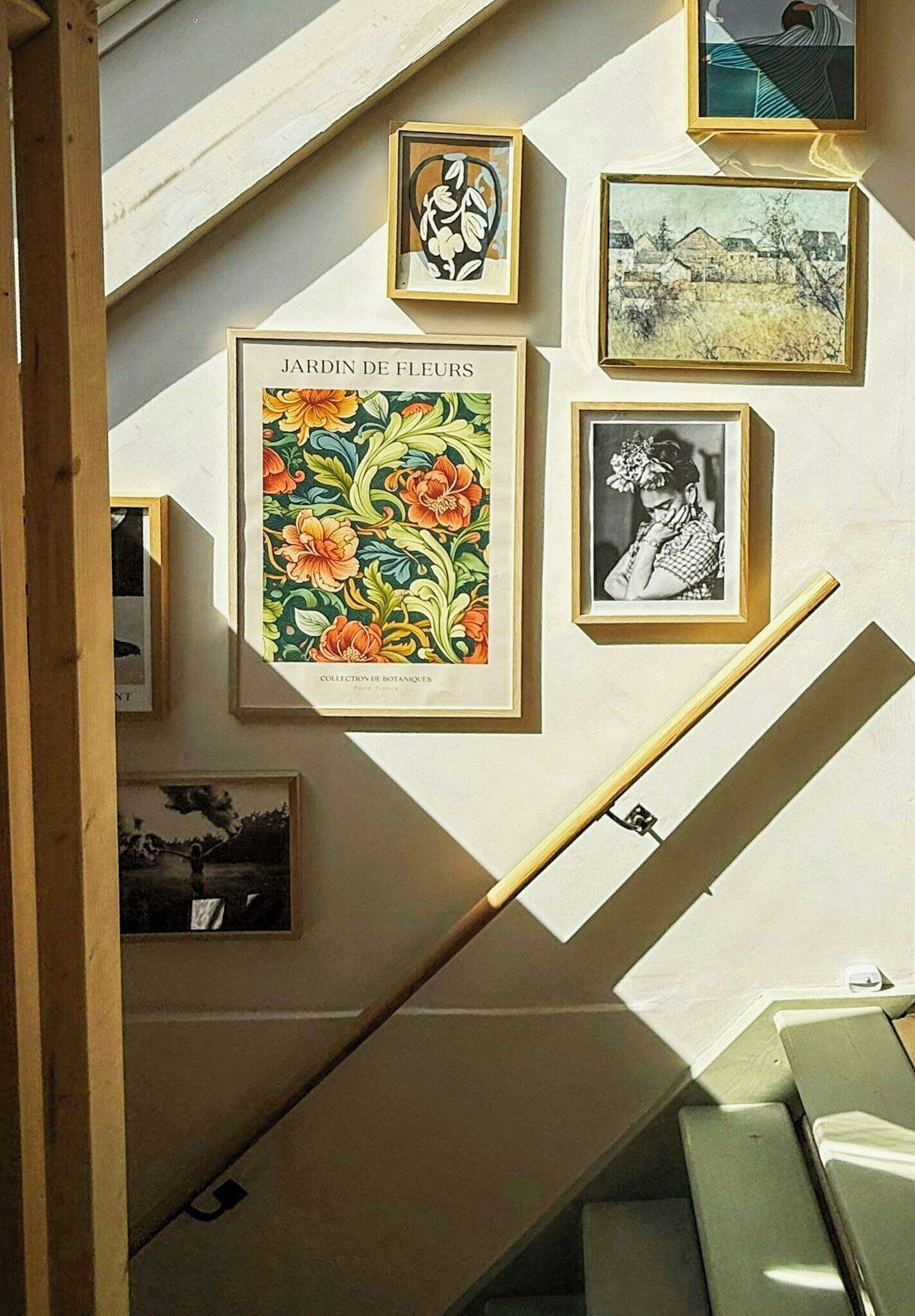 Una escalera con barandilla, rodeada de impresiones y fotografías botánicas enmarcadas en las paredes.