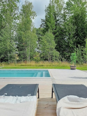 A poolside area with two lounge chairs, a wooden deck, and a pool.