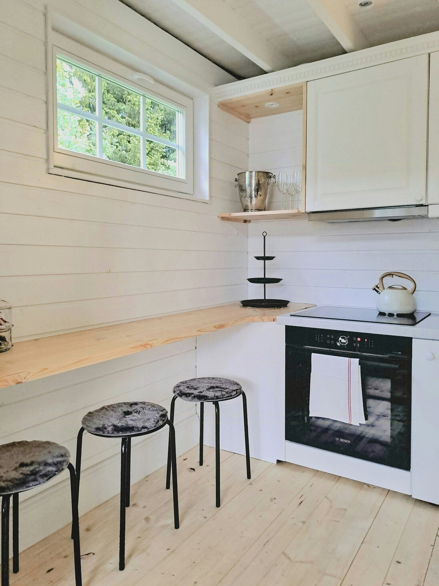A kitchen with white cabinets, a wooden countertop, a Bosch oven, and three bar stools.
