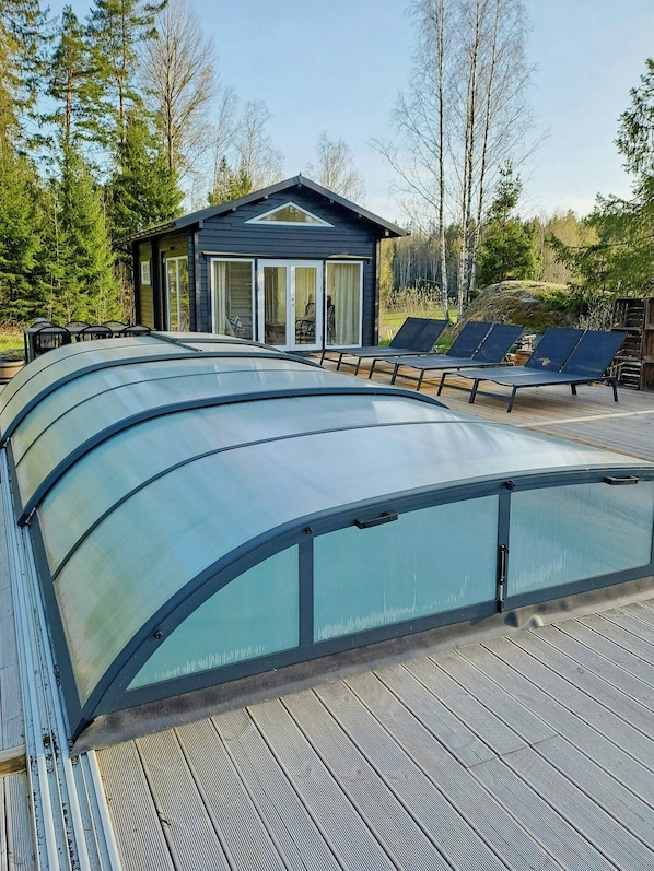 A modern building with a glass conservatory, outdoor seating, and a natural forest backdrop.