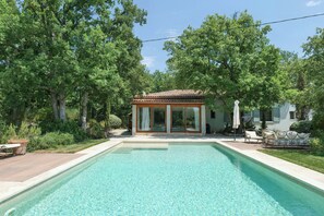 Ein Swimmingpool mit überdachter Terrasse, umgeben von Bäumen und einem Haus.