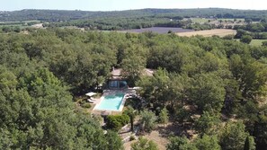 Eine Vogelperspektive zeigt ein Anwesen mit Swimmingpool, umgeben von dichter Vegetation, ein großes Haus mit Terrasse und Blick auf die umliegende Landschaft.
