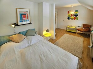 Ein Schlafzimmer mit einem Bett, Nachttischlampen, einem Sessel, einem kleinen Tisch und einem Wandbild.