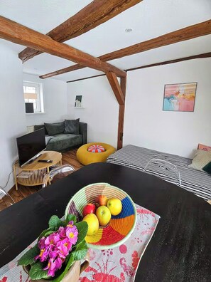 Ein Wohnzimmer mit einem schwarzen Tisch, einer Couch, einem gelben Sitzsack, einem Fernseher und einem Gemälde an der Wand.