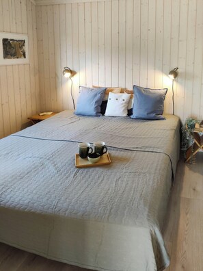 Un letto con copriletto trapuntato, lampade sui comodini e un vassoio con tazze e una ciotola.