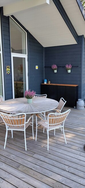 Una terrazza con un tavolo rotondo e sedie, una porta in vetro e due piante in vaso.