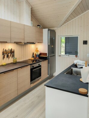 Eine moderne Küche mit Holzschränken, einem Edelstahlkühlschrank und einer schwarzen Arbeitsplatte.