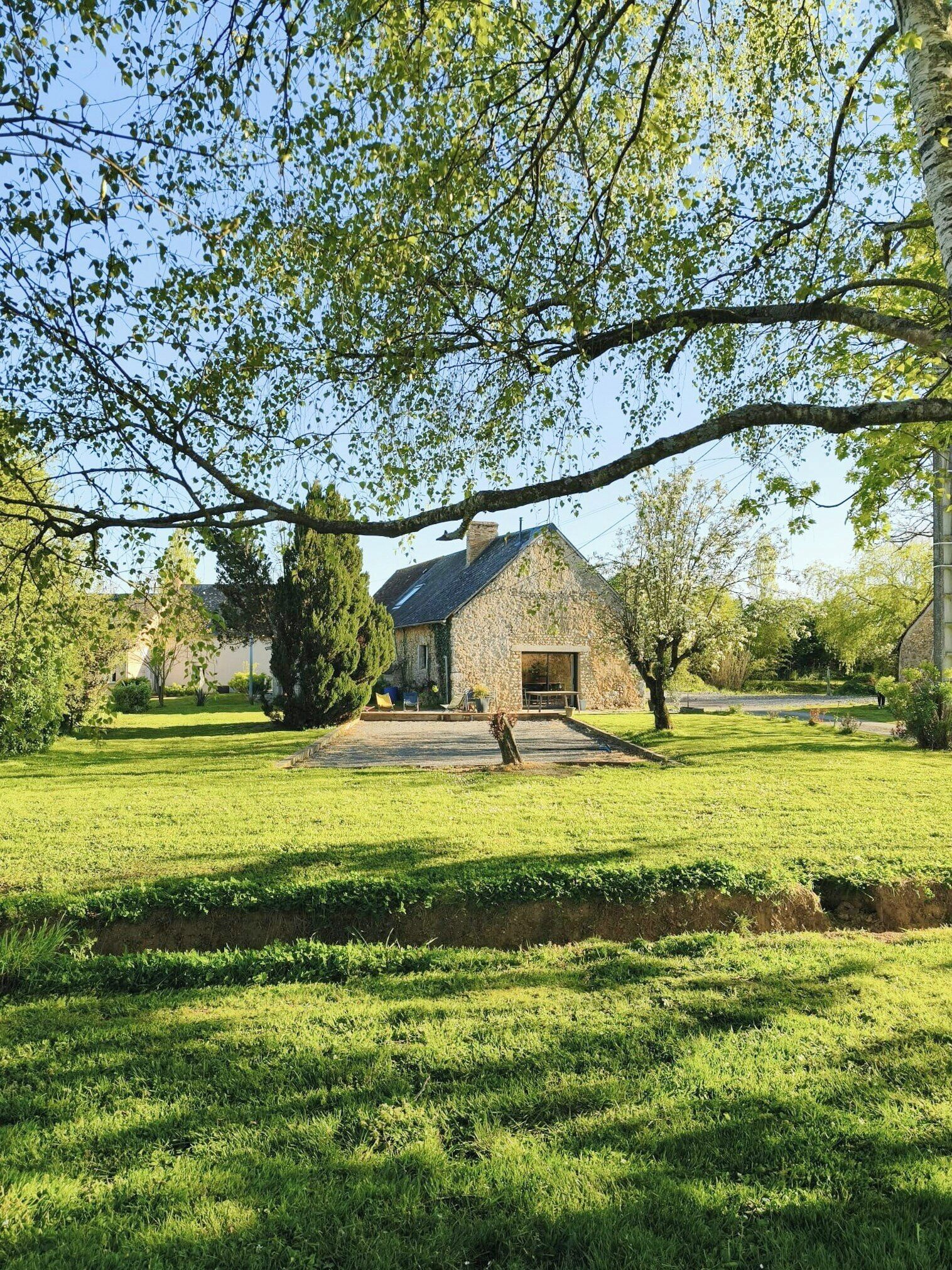 A stone house with a chimney, surrounded by a well-maintained lawn and trees.