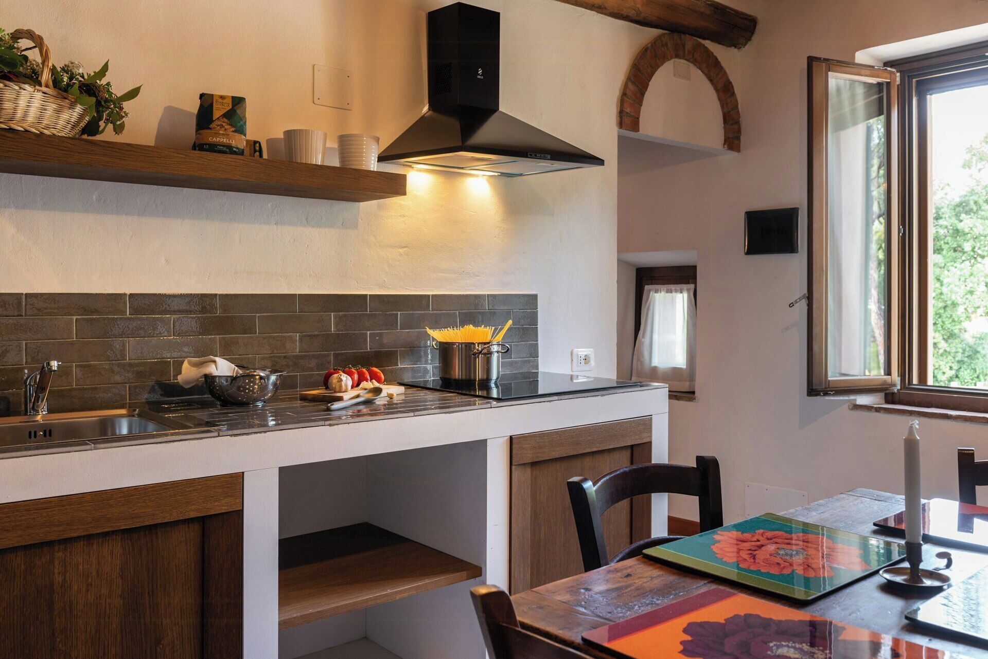 A kitchen with a black range hood, a window with curtains, and a table with a floral tablecloth.