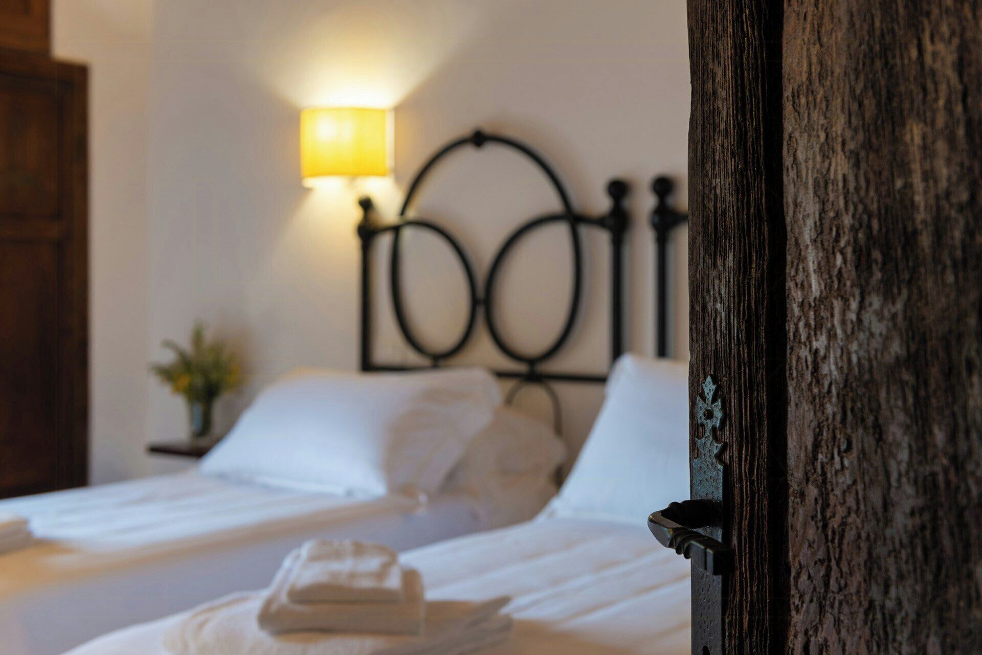 Een bed met witte lakens, een bedlampje en een houten hoofdbord.
